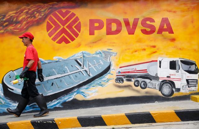 A worker walks past a mural with a PDVSA logo at its gas station in Caracas