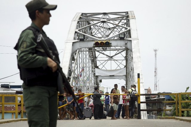 People stand next to a closed gate while a Venezuelan soldier stands guard at La Union international bridge, on the border with Colombia at Boca de Grita in Tachira state, Venezuela
