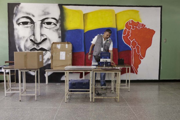 A worker of the National Electoral Council (CNE) configures a voting machine in front of a mural depicting Venezuela's late President Hugo Chavez at a school in Caracas, December 4, 2015. Venezuela will hold parliamentary elections on December 6. REUTERS/Marco Bello   FOR EDITORIAL USE ONLY. NO RESALES. NO ARCHIVE.