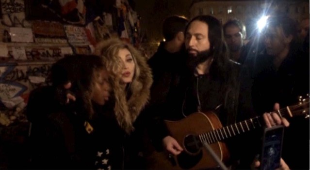 A still image from a video shows singer Madonna (C) giving an impromptu street concert at the Place de la Republique in Paris December 10, 2015, the site of massed tributes for the victims of the recent Paris attacks. Madonna performed John Lennon's 'Imagine' and her song 'Ghosttown', accompanied just by a guitar in the middle of the cold night.  REUTERS TV
