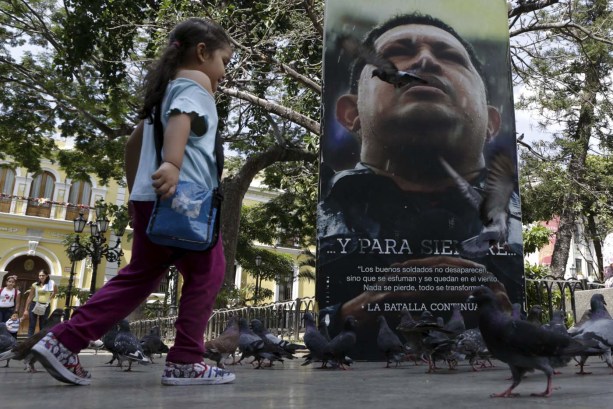 A girl runs among pigeons next to a portrait of Venezuela's late President Hugo Chavez at the Plaza Bolivar near the building housing the National Assembly in Caracas, January 8, 2016. REUTERS/Marco Bello