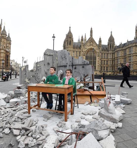 FOTOGRAFÍA EMBARGADA HASTA LAS 0001 DEL 4 DE FEBRERO DE 2016 FA004 LONDRES (REINO UNIDO) 03/02/2016.- Los pequeños Abdalá (izda), de 12 años, y Dania (dcha), de 10, se sientan en un pupitre instalado en una recreación de su colegio bombardeado en Alepo (Siria) a las puertas del Parlamento en Londres (Reino Unido) durante un evento organizado por Save the Children para concienciar sobre la importancia de la educación para los niños refugiados hoy, 3 de febrero de 2016. El evento se ha celebrado con motivo de la conferencia de donantes de Siria que se celebra mañana en Londres. EFE/Facundo Arrizabalaga