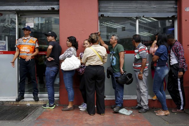 A police officer stands guard at the door while people form a line to try to buy cornmeal flour and margarine at a pharmacy in Caracas March 15, 2016. REUTERS/Carlos Garcia Rawlins