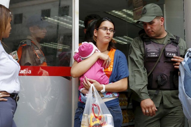 A Venezuelan soldier stands guard at the door while a woman carrying her baby leaves a pharmacy after buying basic goods in Caracas March 15, 2016. REUTERS/Carlos Garcia Rawlins