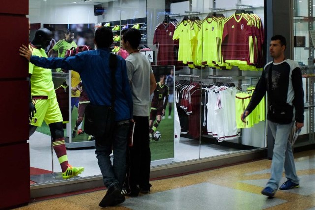 People look at a mannequin dressed in the Venezuelan national football team alternative uniform at a mall in Caracas, on June 16, 2016. Supporting the national football team has become expensive for Venezuelans. / AFP PHOTO / FEDERICO PARRA / TO GO WITH AFP STORY BY ESTEBAN ROJAS