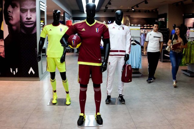 People walk past a mannequin dressed in the Venezuelan national football team uniform at a mall in Caracas, on June 16, 2016. Supporting the national football team has become expensive for Venezuelans. / AFP PHOTO / FEDERICO PARRA / TO GO WITH AFP STORY BY ESTEBAN ROJAS