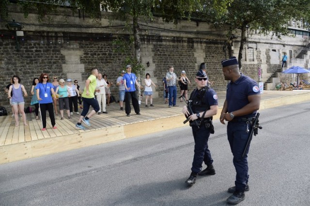 Policemen walk as people exercise on "Paris Plage" (Paris Beach) on the bank of the Seine river, in central Paris, on July 20, 2016 during the opening day of the event. The 15th edition of Paris Plage will run until September 4, 2016. / AFP PHOTO / BERTRAND GUAY