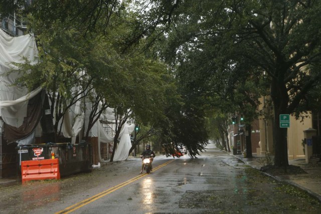 CHARLESTON, SC - OCTOBER 8: A motorist on a scooter drives around a nearly-fallen tree in the wake of Hurricane Matthew on October 8, 2016 in Charleston, South Carolina. Across the Southeast, Over 1.4 million people have lost power due to Hurricane Matthew which has been downgraded to a category 1 hurricane on Saturday morning. Brian Blanco/Getty Images/AFP