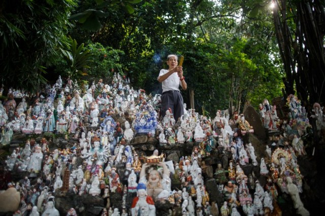 In this picture taken on August 9, 2016 dedicated volunteer Wong Wing-pong, an 85 year old retired butcher, offers incense to unwanted statues of deities, gathered and repaired after their owners discarded them, on a rocky slope running down to the sea in Hong Kong. Religion and local customs permeate Hong Kong, where Buddhist and Taoist temples are common and incense offerings are regularly burned outside local businesses. Private homes often have a shrine to a local deity, with Christian churches and mosques also in the mix. But with space at a premium in a city were rents are sky high, informal collections of discarded gods often decorate roadsides and public spaces. / AFP PHOTO / Anthony WALLACE / To go with "HONG KONG-CULTURE-LIFESTYLE-RELIGION", FEATURE by Dennis Chong