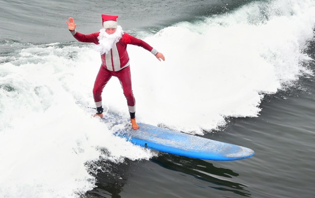 Surfing Santa, Michael Pless, waves while riding a wave at Seal Beach, California, on December 10, 2016, where he runs a surfing school and has every December since in 1990's gone out to surf in his Santa Claus outfit. / AFP PHOTO / Frederic J. BROWN