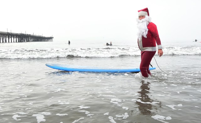 Surfing Santa, Michael Pless, makes his way out to surf at Seal Beach, California on December 10, 2016, where he runs a surfing school and has every December since in 1990's gone out to surf in his Santa Claus outfit. / AFP PHOTO / Frederic J. BROWN