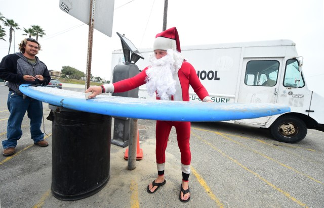 Surfing Santa, Michael Pless, waxes his board before catching a wave at Seal Beach, California on December 10, 2016, where he runs a surfing school and has every December since in 1990's gone out to surf in his Santa Claus outfit. / AFP PHOTO / Frederic J. BROWN