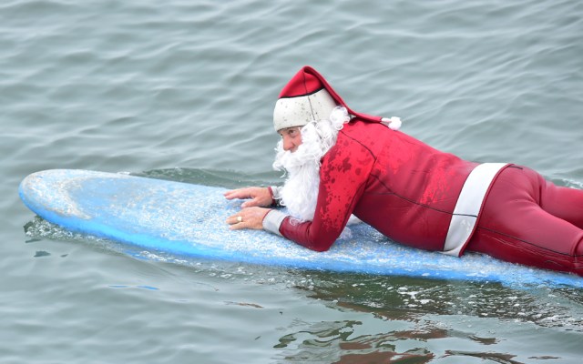 Surfing Santa, Michael Pless, lays on his board making his way out to catch a wave at Seal Beach, California on December 10, 2016, where he runs a surfing school and has every December since in 1990's gone out to surf in his Santa Claus outfit. / AFP PHOTO / Frederic J. BROWN