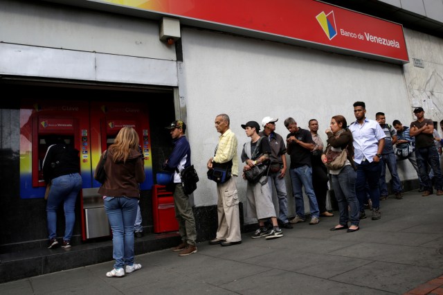 People line up to withdraw cash from an automated teller machine (ATM) outside a Banco de Venezuela branch in Caracas, Venezuela December 12, 2016. REUTERS/Marco Bello