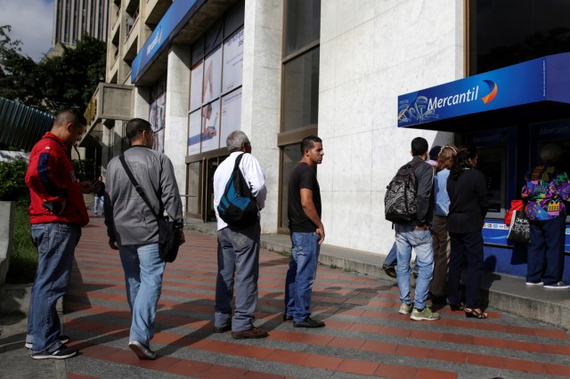 People line up to withdraw cash from an automated teller machine (ATM) outside a Banco Mercantil branch in Caracas, Venezuela December 12, 2016. REUTERS/Marco Bello