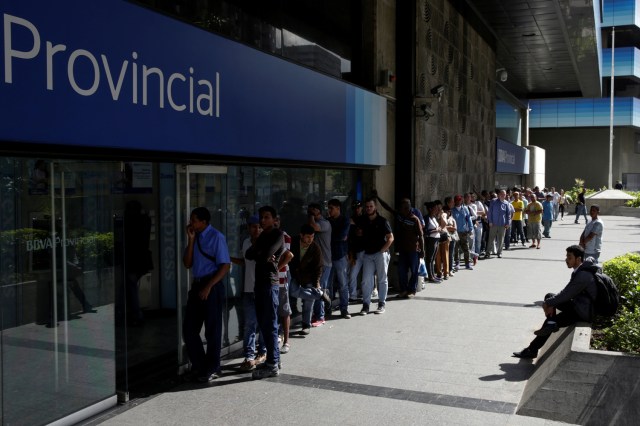 People line up to withdraw cash from an automated teller machine (ATM) outside a Banco Provincial branch in Caracas, Venezuela December 12, 2016. REUTERS/Marco Bello