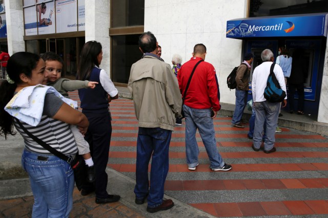 People line up to withdraw cash from an automated teller machine (ATM) outside a Banco Mercantil branch in Caracas, Venezuela December 12, 2016. REUTERS/Marco Bello