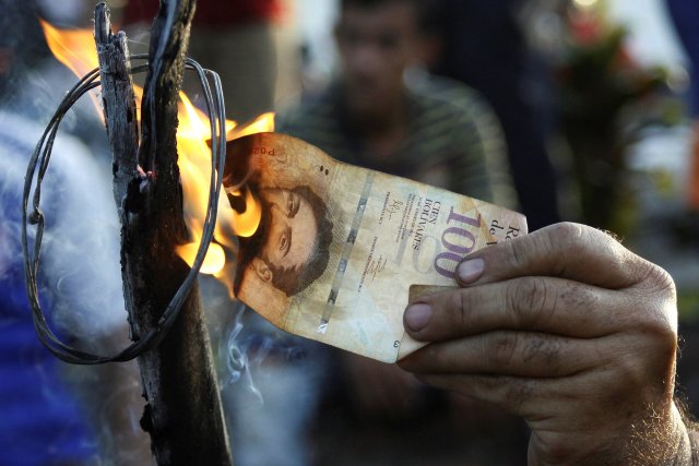 A man burns a 100-bolivar bill during a protest in El Pinal, Venezuela December 16, 2016. REUTERS/Carlos Eduardo Ramirez