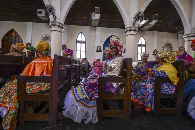 Women dressed as "madamas" attend a mass before the beginning of the Carnival in El Callao, in Bolivar state, Venezuela on February 26, 2017.  El Callao's carnival was recently named Unesco's Intangible Cultural Heritage of Humanity and is led by the madamas, the pillars of Callaoense identity representing Antillean matrons considered the communicators of values, who dance and wear colourful dresses. / AFP PHOTO / JUAN BARRETO