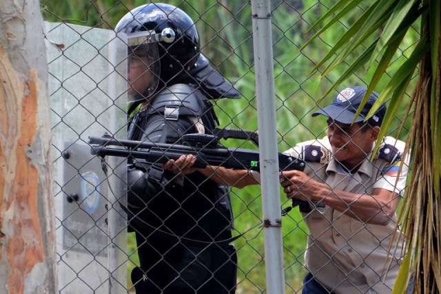 A policeman aims a shotgun at students opposing Venezuelan President Nicolas Maduro demonstrating in San Cristobal, Venezuela on April 5, 2017. University students and police clashed Wednesday during a protest in the Venezuelan city of San Cristobal (western border with Colombia), with a balance of at least a dozen injured. / AFP PHOTO / George Castellanos