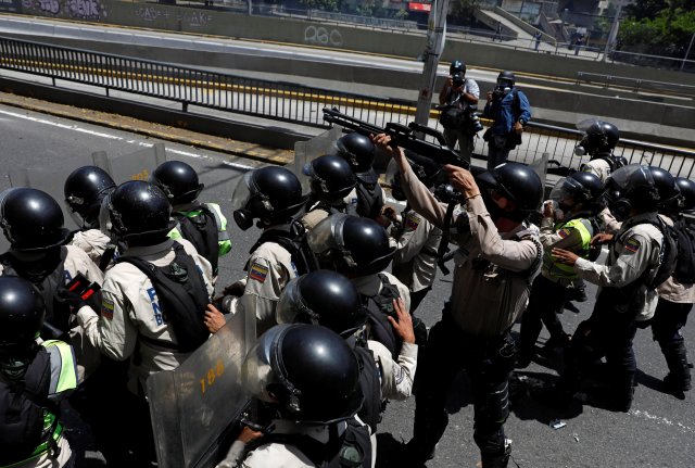 A riot police officer holds a weapon in the direction of demonstrators during an opposition rally in Caracas, Venezuela