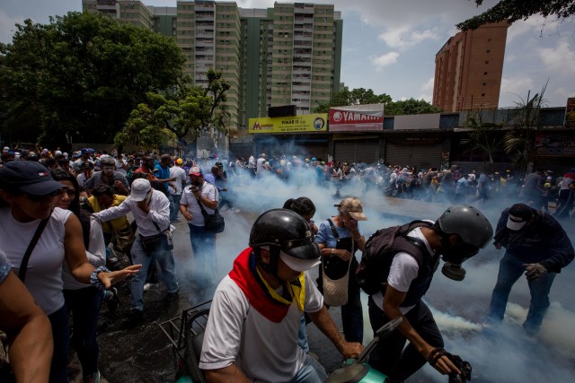CAR012. CARACAS (VENEZUELA),19/04/2017 - Manifestantes se protegen de los gases lacrimógenos durante una protesta en contra del Gobierno venezolano hoy, miércoles 19 de abril de 2017, en Caracas (Venezuela). La policía disolvió hoy con gases lacrimógenos una de las marchas opositoras en el centro de Caracas que pretendía llegar a la sede de la Defensoría del Pueblo, mientras que desde otra de las concentraciones antichavistas en esa zona de la ciudad se reportó una persona muerta. EFE/MIGUEL GUTIERREZ