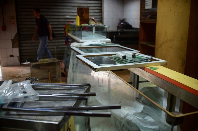 A man picks up the mess at a business in Caracas on April 20, 2017 a day after looting occurred after demonstrations pro and against the government of Venezuelan President Nicolas Maduro. Venezuelan riot police fired tear gas Thursday at groups of protesters seeking to oust Maduro, who have vowed new mass marches after a day of deadly unrest. On the eve, hundreds of thousands of people fed up with food shortages and demanding elections joined protest marches in Caracas and several other cities while thousands of Maduro's supporters held a counter-rally in central Caracas.  / AFP PHOTO / Ronaldo SCHEMIDT