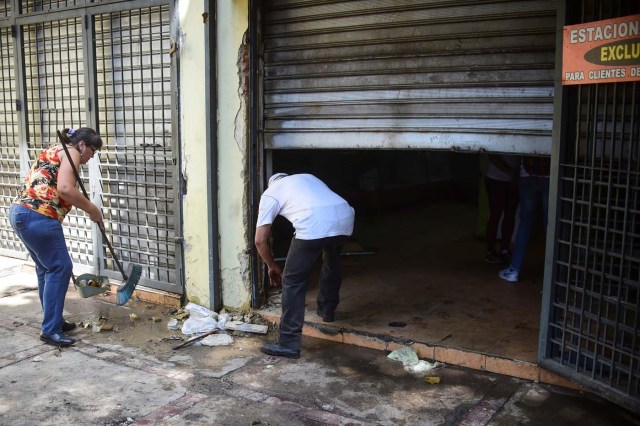 A woman sweeps the sidewalk in Caracas on April 20, 2017 a day after businesses were looted after demonstrations pro and against the government of Venezuelan President Nicolas Maduro. Venezuelan riot police fired tear gas Thursday at groups of protesters seeking to oust Maduro, who have vowed new mass marches after a day of deadly unrest. On the eve, hundreds of thousands of people fed up with food shortages and demanding elections joined protest marches in Caracas and several other cities while thousands of Maduro's supporters held a counter-rally in central Caracas.  / AFP PHOTO / Ronaldo SCHEMIDT