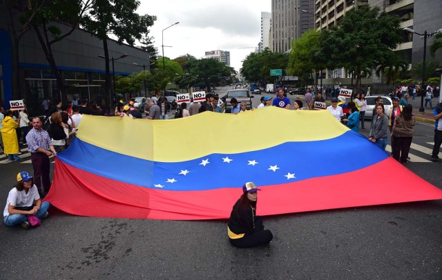 Demonstrators display a Venezuelan national flag as they block a street during a protest against Venezuelan President Nicolas Maduro in Caracas, on May 2, 2017. Venezuelan President Nicolas Maduro called for a new constitution Monday as he fights to quell a crisis that has led to more than a month of protests against him and deadly street violence. The opposition slammed the tactic as a "coup d'etat" and urged protesters to "block the streets" from Tuesday. It said it was organizing a "mega protest" for Wednesday. / AFP PHOTO / RONALDO SCHEMIDT