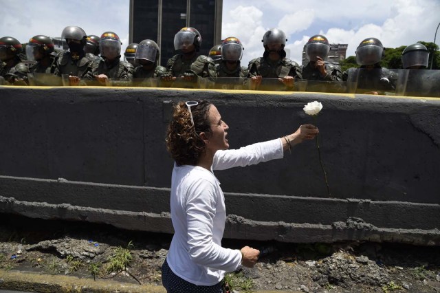 A Venezuelan opposition activist offers a flower to members of the Bolivarian National Guard standing guard during a women's march aimed to keep pressure on President Nicolas Maduro, whose authority is being increasingly challenged by protests and deadly unrest, in Caracas on May 6, 2017. The death toll since April, when the protests intensified after Maduro's administration and the courts stepped up efforts to undermine the opposition, is at least 36 according to prosecutors. / AFP PHOTO / JUAN BARRETO