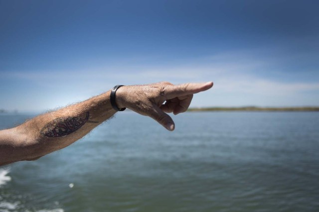 Mayor and waterman James Eskridge's tattoo of the Jesus fish adorns his arm as he points out areas that have been completely eroded away in Tangier, Virginia, May 16, 2017, where climate change and rising sea levels threaten the inhabitants of the slowly sinking island. Now measuring 1.2 square miles, Tangier Island has lost two-thirds of its landmass since 1850. If nothing is done to stop the erosion, it may disappear completely in the next 40 years. / AFP PHOTO / JIM WATSON