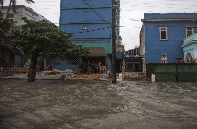 Locals sit on the pavement in a flooded street during the passage of Hurricane Irma in Havana, on September 9, 2017. Irma's blast through the Cuban coastline weakened it to a Category Three, but it is still packing winds of 125 miles (200 kilometer) per hour. / AFP PHOTO / YAMIL LAGE