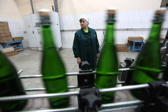 An employee stands as she works on the production line in the "Artwinery" winery firm in the eastern Ukrainian city of Bakhmut on July 12, 2017. The winery is located in a government-held town just two dozen kilometres (15 miles) from the frontline in Ukraine's low-level war, where the army and Russian-backed rebels continue to lob deadly artillery barrages at each other. The town spent around a month under rebel control in 2014, and in 2015 the frontline was so close that the town came under rebel shelling. But despite more than three years of fighting that has claimed some 10,000 lives, Nasyrov's employer, Artwinery, has never stopped production. / AFP PHOTO / Aleksey FILIPPOV