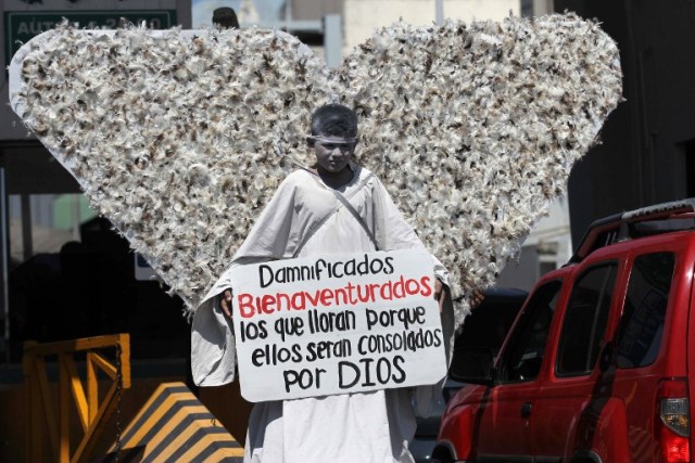 A member of Christian church Salmo 100 dressed as an angel shows a message addressed to the victims of the last earthquake in Mexico City, in front of drivers crossing the Cordova-Americas International Bridge between Ciudad Juarez, Chihuahua state and El Paso, Texas on September 23, 2017 in Ciudad Juárez, Chihuahua, Mexico. / AFP PHOTO / HÉRIKA MARTÍNEZ