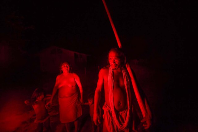 Chieftain Akaupotyr Waiapi walks with his family holding a flute, at night in the Manilha village in Waiapi indigenous reserve in Amapa state in Brazil on October 14, 2017.  Tribal chieftain Tzako Waiapi perfectly remembers the day almost half a century ago when his hunting party stumbled across a group of white adventurers in the Amazon rainforest. Within months, nearly everyone in his entire tribe had died from disease.  / AFP PHOTO / Apu Gomes / TO GO WITH AFP STORY "When the Waipai tribe almost died out" by Sebastian Smith
