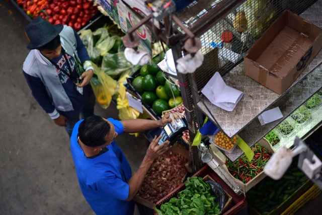 A man pays for groceries at the municipal market of Chacao in Caracas on November 2, 2017. This week, Venezuelan President Nicolas Maduro introduced a new bank note of 100,000 Bolivars - five times the current largest denomination - and announced a 30 percent minimum wage hike. / AFP PHOTO / FEDERICO PARRA