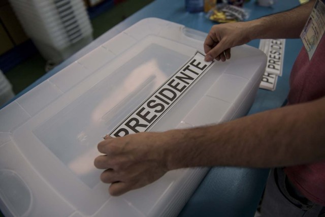 A man places a sticker reading "President" on a ballot box as polling stations are being set up at the National Stadium in Santiago on November 18, 2017 on the eve of Chile's general elections. After four years of socialist rule, Chile is expected to revert to the right in elections Sunday, with Sebastian Pinera set to return as president, confirming a shift to conservative leaders across Latin America. Opinion polls make Pinera, a 67-year-old billionaire businessman sometimes referred to as "Chile's Berlusconi", the hot favourite to return to the presidency he occupied from 2010-2014.  / AFP PHOTO / Martin BERNETTI