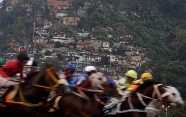 Competitors take part in a horserace, with a slum or "barrio" in the background at La Rinconada Hippodrome, Caracas, Venezuela, October 8, 2017. REUTERS/Ricardo Moraes SEARCH "MORAES GAMBLING" FOR THIS STORY. SEARCH "WIDER IMAGE" FOR ALL STORIES. TPX IMAGES OF THE DAY.