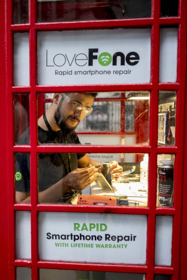 Fouad Choaibi works inside a red telephone box from which he runs a smartphone repair shop on Southhampton Row, in central London on October 20, 2017. Facing extinction due to ubiquitous mobile phones, Britain's classic red telephone boxes are being saved from death row by ingenious conversions into all sorts of new uses. / AFP PHOTO / Tolga Akmen / TO GO WITH AFP STORY 'Britain-heritage-business' by Martine PAUWELS