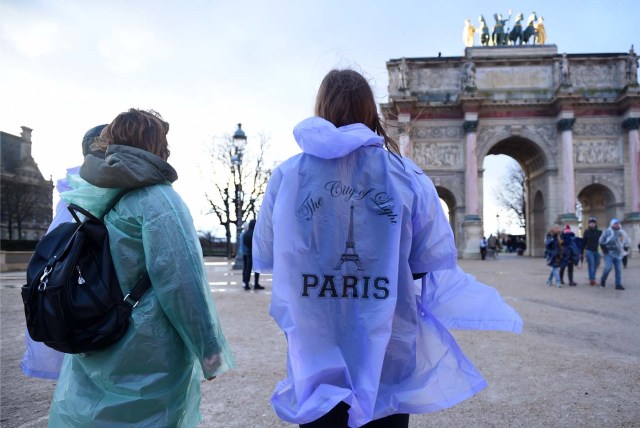 Tourists wearing raincoats stand by the Arc de Triomphe du Carrousel monument by the Louvre Museum on January 1, 2018 in Paris. / AFP PHOTO / GUILLAUME SOUVANT