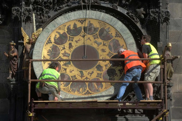 (FILES) This file photo taken on May 25, 2017 shows clockmaker Petr Skala (C) removing the calendar dial of Prague's medieval astronomical clock (Prazsky orloj), during the ongoing renovation of the Old Town Hall at the Old Town Square in Prague. The Prazsky orloj, the third-oldest astronomical clock in the world, will be dismantled from January 8, 2018, for a six-month renovation. / AFP PHOTO / Michal Cizek