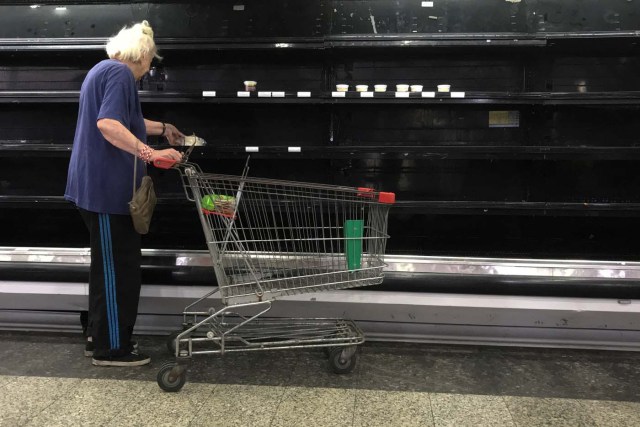 A woman selects goat cheese from partially empty refrigerators at a supermarket in Caracas, Venezuela January 10, 2018. REUTERS/Marco Bello