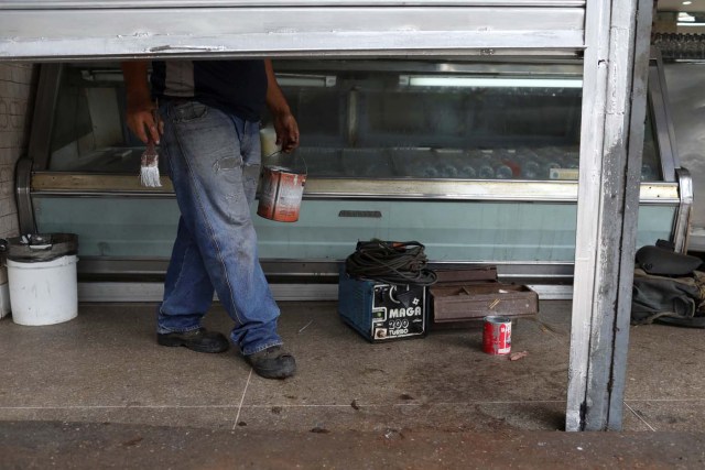 A worker paints a security shutter after repairing it at a bakery in Caracas, Venezuela January 16, 2018. Picture taken January 16, 2018. REUTERS/Marco Bello