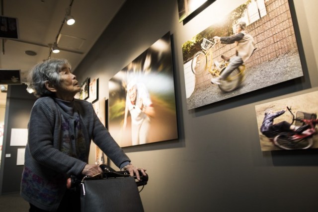 In this picture taken on December 14, 2017, Kimiko Nishimoto looks at her pictures on the opening day of her photo exhibition in Tokyo. The madcap Japanese great-grandmother armed with a camera and an appetite for mischief has shot to fame for taking side-splitting selfies -- many of which appear to put her in harm's way. / AFP PHOTO / Behrouz MEHRI / TO GO WITH Japan-lifestyle-photography-offbeat-senior-citizens,FEATURE by Alistair HIMMER