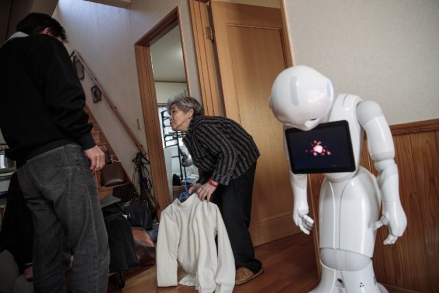 In this picture taken on January 16, 2018, Kimiko Nishimoto consults with her son Kazutami to select a costume for a photoshoot as her humanoid robot called Pepper (R) is seen at her house in the western Japanese city of Kumamoto. The madcap Japanese great-grandmother armed with a camera and an appetite for mischief has shot to fame for taking side-splitting selfies -- many of which appear to put her in harm's way. / AFP PHOTO / Behrouz MEHRI / TO GO WITH Japan-lifestyle-photography-offbeat-senior-citizens,FEATURE by Alistair HIMMER