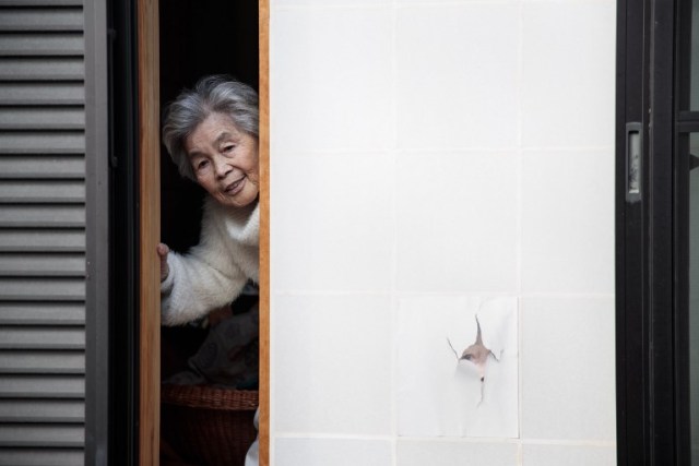 In this picture taken on January 16, 2018, Kimiko Nishimoto poses next to a picture of her on the sliding window of her house in the western Japanese city of Kumamoto. The madcap Japanese great-grandmother armed with a camera and an appetite for mischief has shot to fame for taking side-splitting selfies -- many of which appear to put her in harm's way. / AFP PHOTO / Behrouz MEHRI / TO GO WITH Japan-lifestyle-photography-offbeat-senior-citizens,FEATURE by Alistair HIMMER