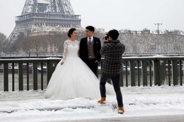 A wedding couple of tourists pose for their own photographer in front of the Eiffel tower on the snow-covered Pont de Bir-Hakeim bridge as winter conditions with snow and freezing temperatures hit in Paris, France, February 7, 2018. REUTERS/John Schults