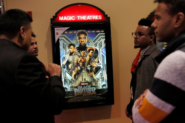 A group of men gather in front of a poster advertising the film "Black Panther" on its opening night of screenings at the AMC Magic Johnson Harlem 9 cinemas in Manhattan, New York, U.S., February 15, 2018.  REUTERS/Andrew Kelly