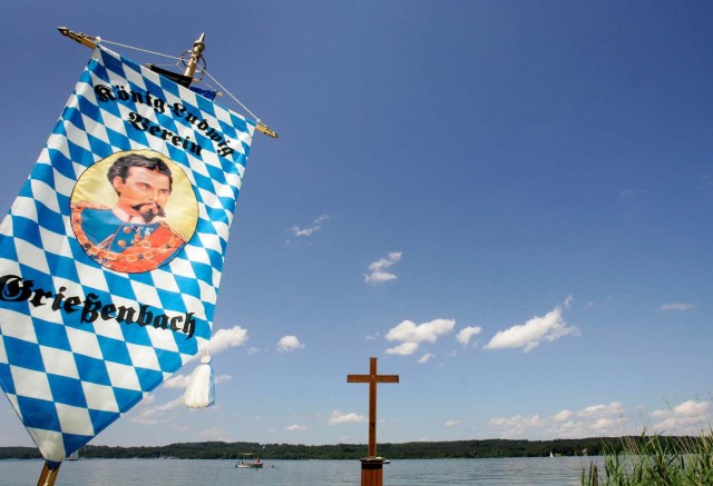 FILE PHOTO: A flag with the picture of King Ludwig II is seen next to the crucifix commemorating the death of the Bavarian King Ludwig II in Berg at lake Starnberg, southern Germany, June 17, 2007. Ludwig II of Bavaria (also known as the Fairy-tale King and Mad King Ludwig), the builder of the famous Neuschwanstein castle, was diagnosed as mentally ill and incarcerated in Berg Castle. On June 13, 1886, his doctor arrived to take him for a walk. A few hours later they were both found drowned in the lake Starnberg. REUTERS/Michaela Rehle/File Photo